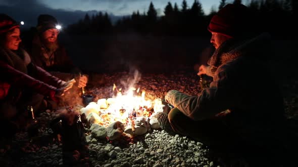 Group of young people sitting at a bonfire at dawn