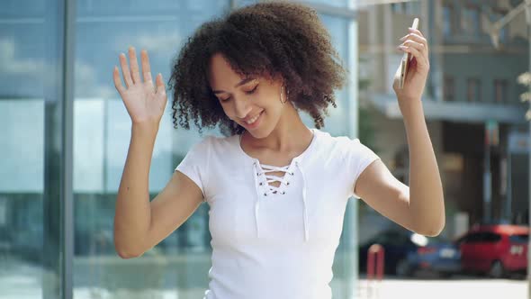 Active African Ethnic Woman Jumping Dancing with Music Holding Smartphone in Street Outdoors. Happy