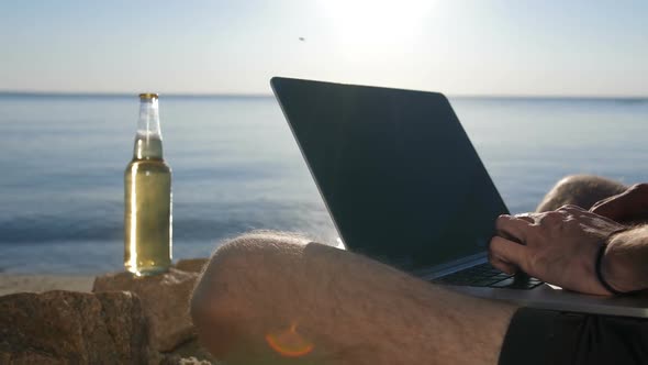 Male Hands Typing Text on Modern Laptop on Beach