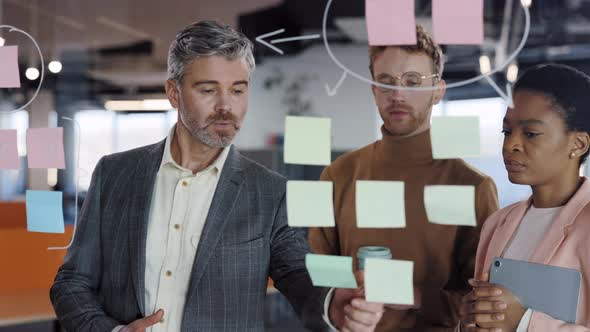 Male Office Worker Putting Stickers on Glass Board and Explaining Concept to Team Members