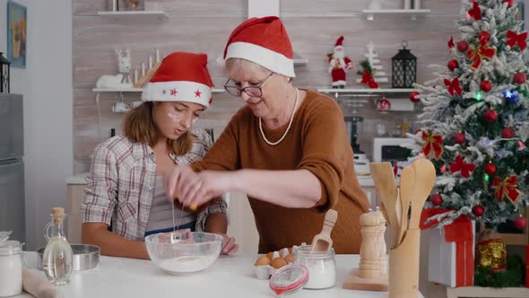 Granddaughter with Granddaughter Breaking Egg in Kitchen Bowl with Flour Ingredient