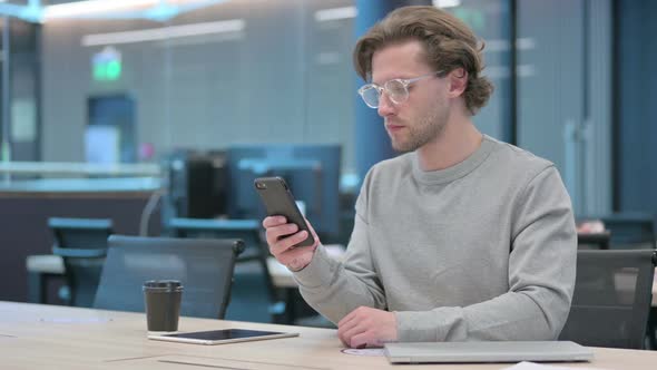 Attractive Young Businessman Using Smartphone in Office