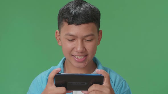 Smiling Young Asian Boy Looking At The Phone Screen In Green Screen In The Studio