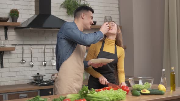 Couple in love preparing vegetarian food in home kitchen, husband feed beloved wife with pizza 