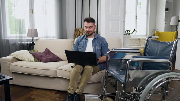 Sedentary Bearded Man Sitting on the Comfortable Couch at Home and Working on Computer