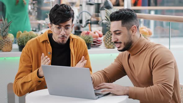 Young Motivated Arab Guy Demonstrates Friend New Application Achievements on Laptop Indian Man