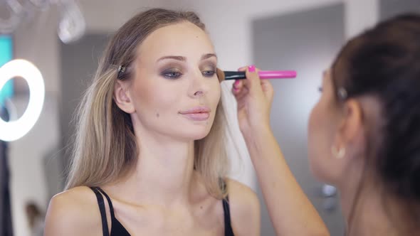 The Makeup Artist Applies the Powder on the Surface of the Young Blonde's Face Slow Mo