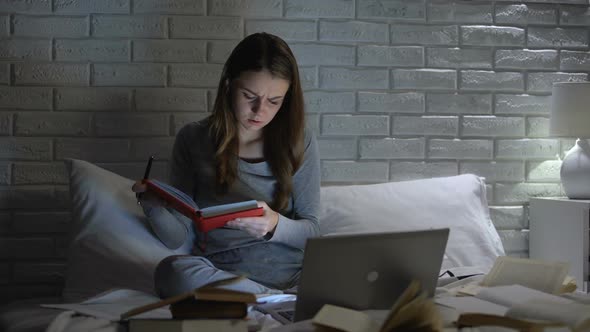 Tired Student Girl Reading Books and Laptop Preparing to Exam Late in Bedroom