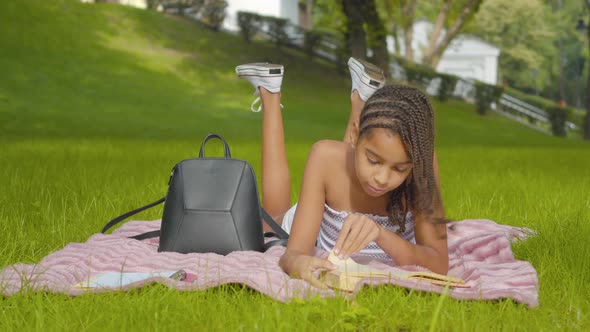 Wide Shot of Absorbed Concentrated Girl Lying on Green Meadow in Park and Reading Book. Portrait of