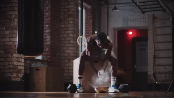 A Black Handsome Man Training in the Gym  Covering Hands in Chalk and Pulling Up Dumbbells