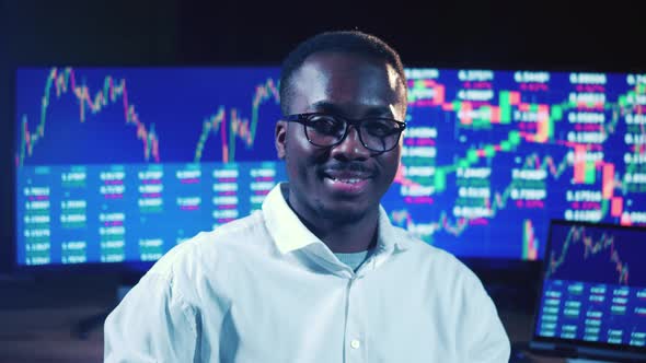 African Stockbroker is Smiling Next to Computer Monitors