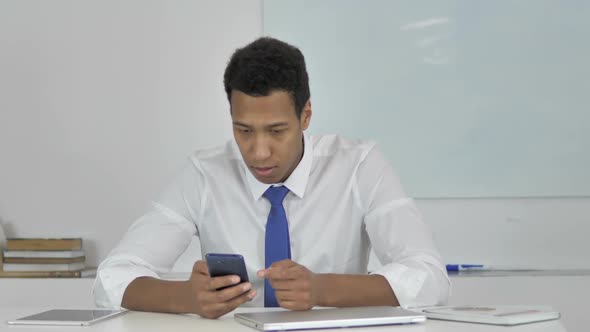 AfroAmerican Businessman Upset for Loss While Using Smartphone
