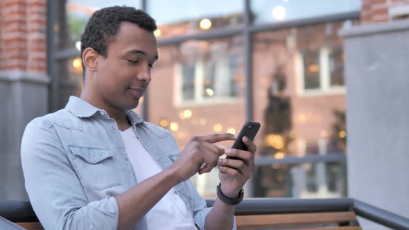 African Man Using Smartphone Sitting Outdoor