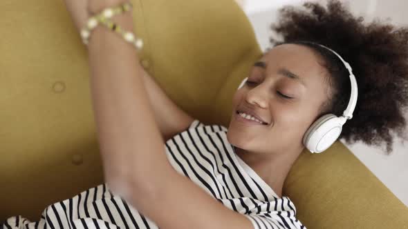 Happy Young African American Woman Lying on Sofa While Listening to Music