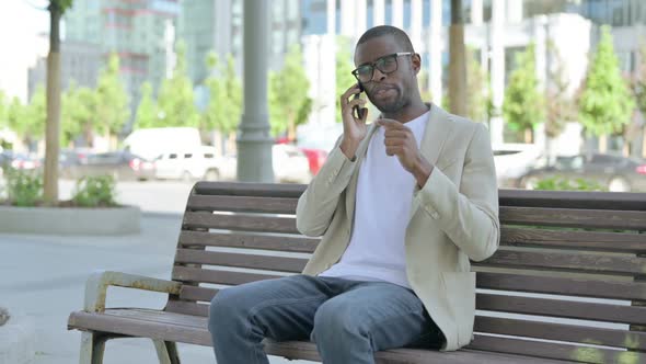 African Man Talking on Phone While Sitting Outdoor on Bench