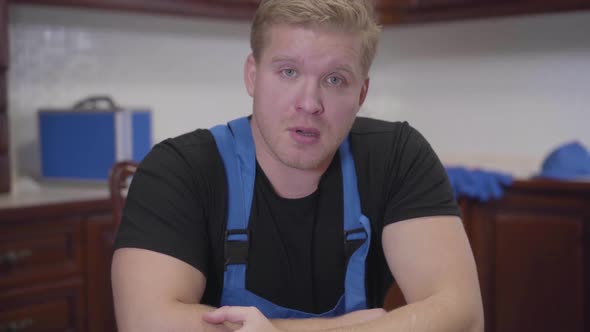 Portrait of Exhausted Caucasian Man with Red Eyes Looking at Camera. Tired Repairman Sitting at