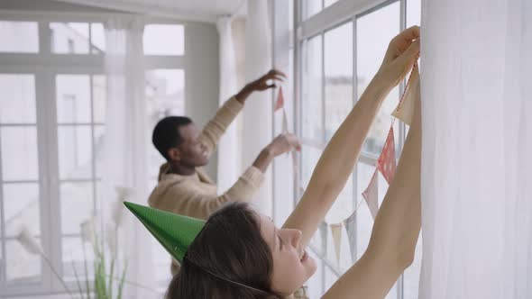 Multinational Couple Hangs Colorful Pennant Banners in Room