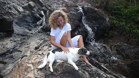 Young Woman Sitting With Her Dog At Waterfall