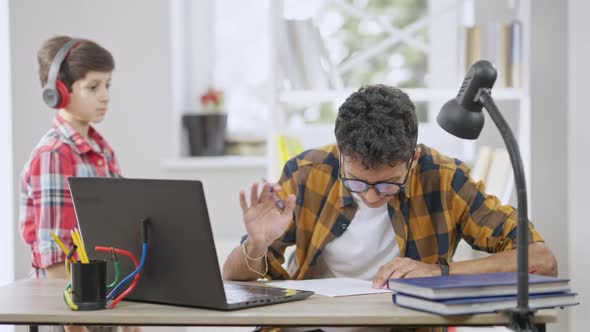 Busy Concentrated Teenage Boy in Eyeglasses Ignoring Little Brother Distracting Student From