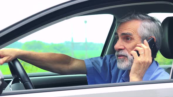 Senior Man Sits in the Car and Calls with Smartphone - Closeup Shot From Side - Countryside