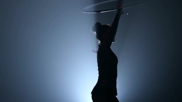 Gymnast Turns the Metal Hoop on the Arm Then on the Leg. Smoke Background. Slow Motion. Silhouette