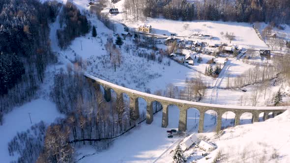 Stone train viaduct railroad around a small village in winter snow.