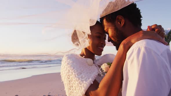 African american couple in love getting married, smiling and looking at other on the beach at sunset