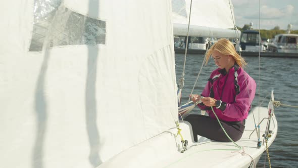 Cute Female Athlete Checks the Ropes Before a Sailing Regatta, Sitting on the Stern of a White Yacht