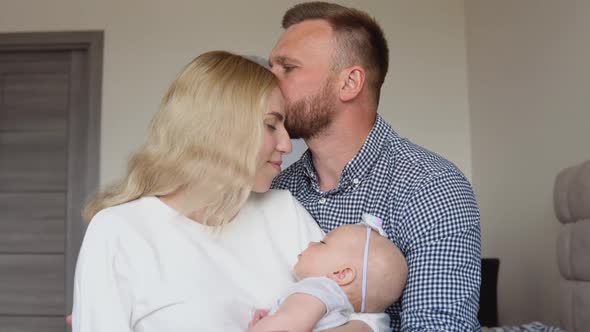 Mother and Father Sit Embracing in the Room While the Child Sleeps in His Mother's Arms