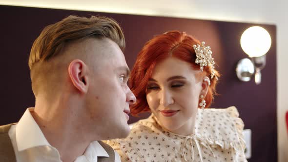 Couple of Man and Woman in Costumes Sit on Bed in Hotel or Apartment and Chat Looking Into Their