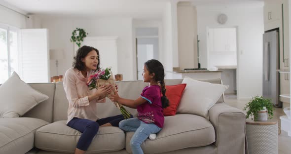 Happy hispanic woman sitting on sofa getting flowers from daughter
