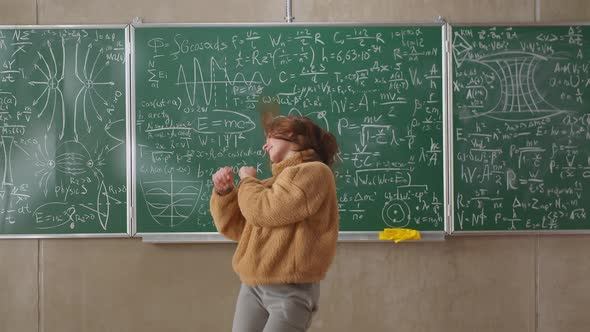 Happy Female Student Dancing in a Classroom at School Against the Background of a Blackboard with