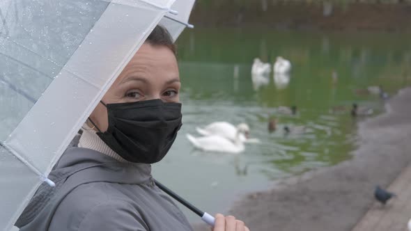 Woman in mask in rainy park. 