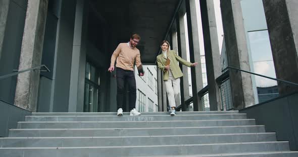 Man and Woman Going Down Stairs in Urban City Center in Smart Casual Business Style, talking