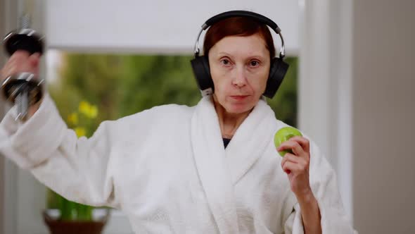 Positive Active Mature Woman Lifting Dumbbell Eating Apple Looking at Camera