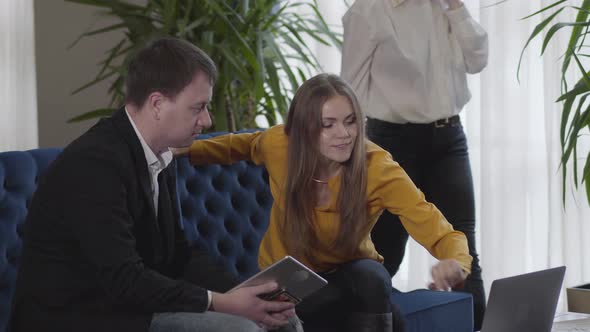 Positive Caucasian Man and Woman Sitting on Couch and Talking As Unrecognizable CEO Walking at the