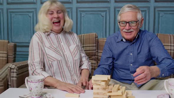 Senior Couple Grandfather Grandmother Resting on Sofa Playing Game with Wooden Blocks at Home