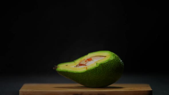 Cutted Avocado at Black Background with Water Droplets Falling in Slow Motion on Tropical Fruit