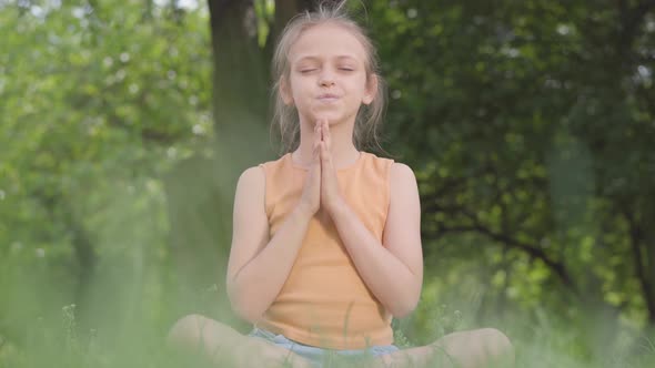 Cute Little Ute Girl Sitting on the Grass Meditating. Child Practices Yoga. Summertime Leisure.