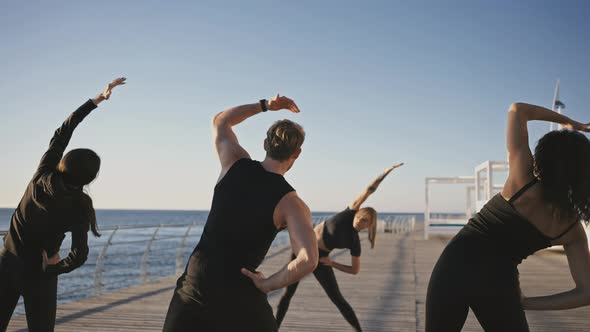 Young Woman Fitness Coach Showing Stretching Exercise to Group of Sporty People Practicing Training