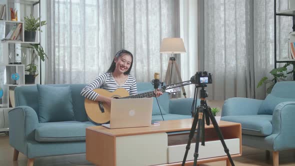 Asian Woman With A Laptop Holding A Guitar And Smiling To Camera While Live Stream At Home