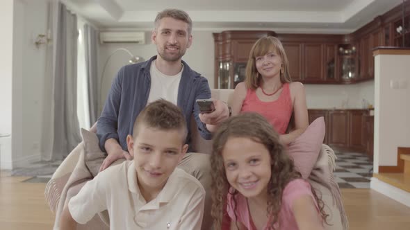 Portrait Young Family Watching TV While Sitting at Home Together. The Father Holds the Remote and