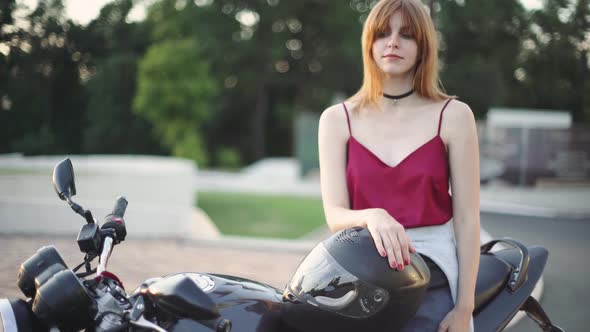 Beautiful Young Redhaired Woman Motorcyclist with Her Motorcycle and Helmet