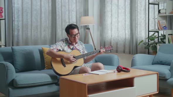 Asian Man Composer With Notebook On Table Playing Guitar At Home