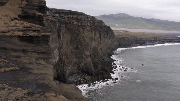 Rocky cliff washed by foamy sea in overcast weather