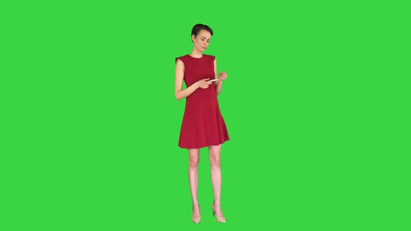 Young Happy Attractive Female in Red Dress Texting on the Phone on a Green Screen, Chroma Key.