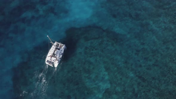 Top down view of luxury catamaran sailboat in turquoise clear water; drone