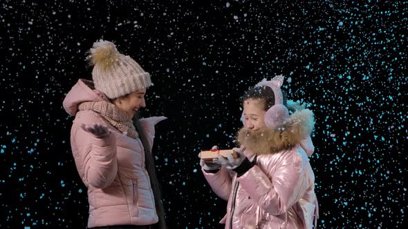 Happy Mom Gives a Gift Box To Her Child. Little Girl Is Happy with the Present and the First Snow