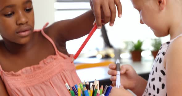 Schoolgirls picking up pencil from pen holder