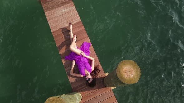 Birds Eye Aerial View of Sexy Young Woman in Pink Dress Lying on Wooden Dock